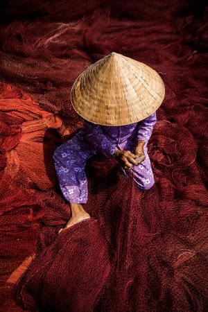 Hoi An artisan weaving a deep maroon fishing net