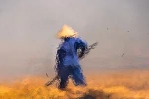 Impressionist photograph of a farmer in a rice field, seen through rising flames, taken by Rehahn in Hoi An.